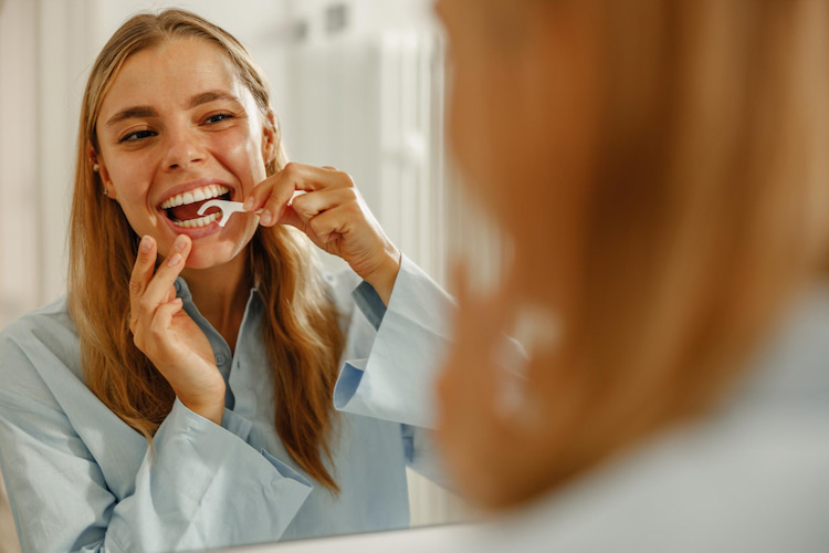 a woman is flossing her teeth to prevent stains after antibiotic use.