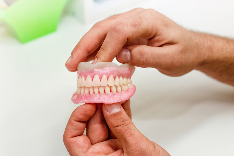 Hands holding a set of dentures and keeping them away from sores and problems.